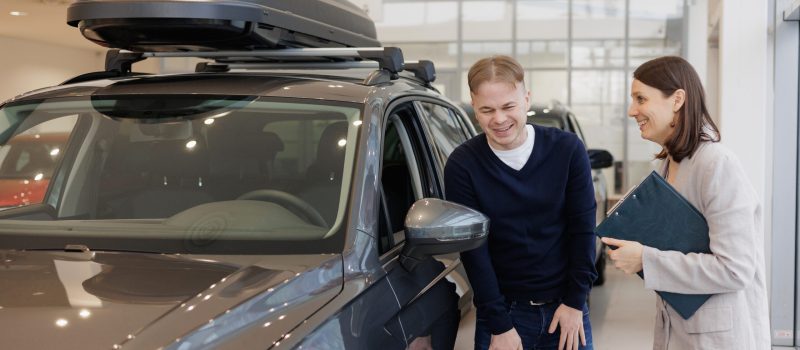man buys a car at a car dealership. A female salesperson and car rental helps with the purchase. signing a trade-in contract and handing over keys, shaking hands. A successful man chooses a new car car. Car rental or repair service center.